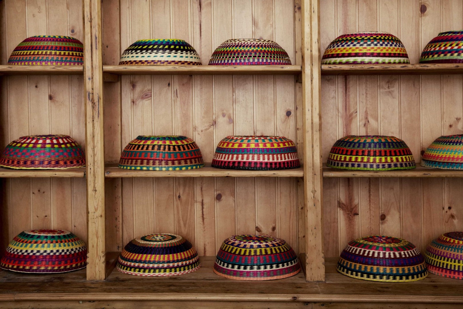 Estantes con sombreros tejidos coloridos en una pared de madera
